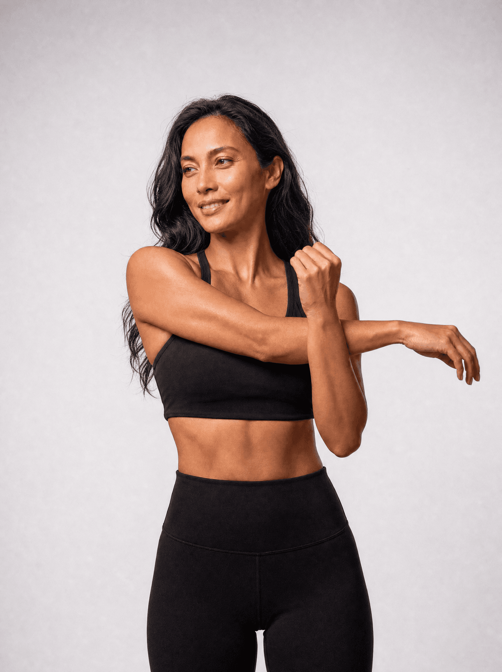 Woman in black athleisure in a shoulder stretch, white studio