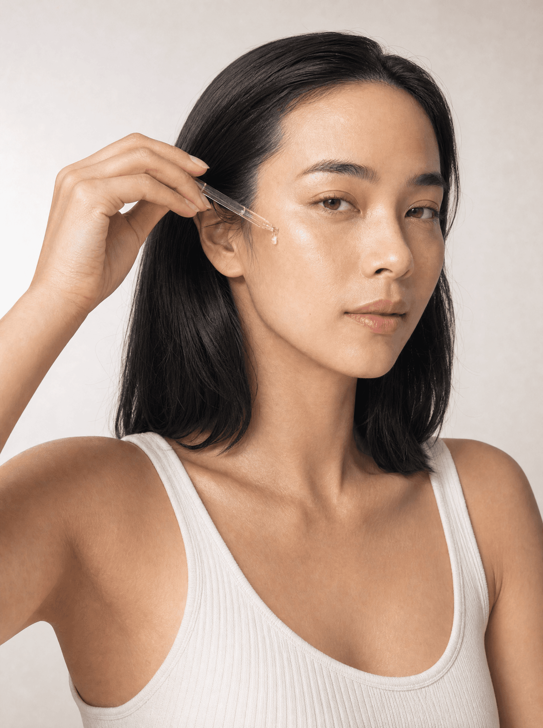 Close beauty portrait, a glass dropper with a single drop above her cheek, white studio